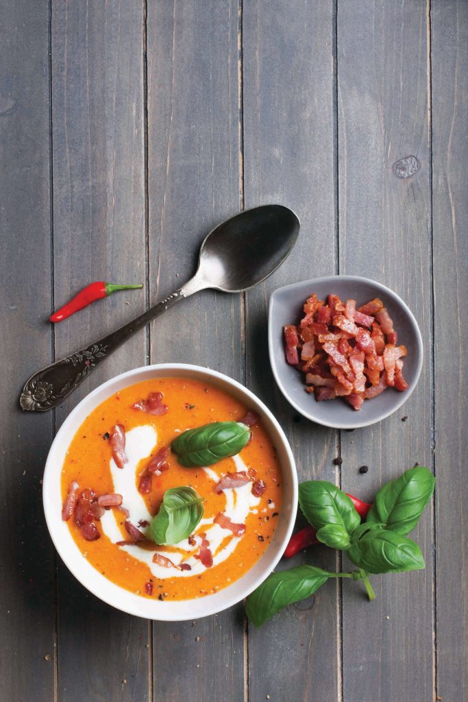 Carrot sweet pepper cream soup with bacon on old wooden background, toned